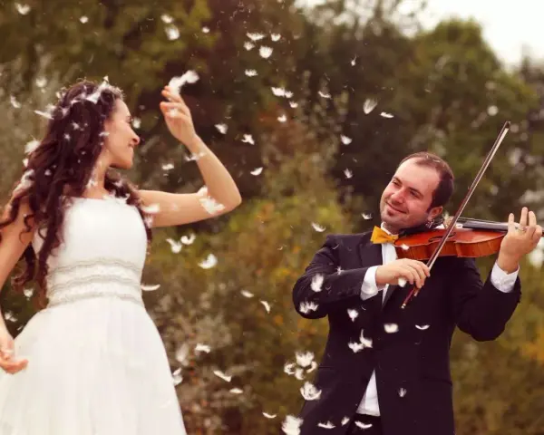 Une mariée en robe blanche danse sous une pluie de plumes, tandis que son mari joue du violon. Une scène féerique pour un mariage champêtre.