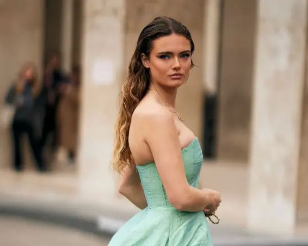 Une jeune femme en robe bustier vert menthe, parfaite pour savoir comment s'habiller pour un mariage. Cheveux longs ondulés, maquillage audacieux.