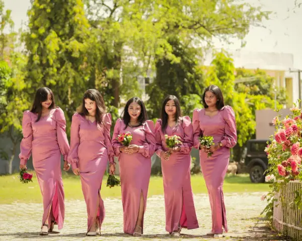 Cinq demoiselles d'honneur en robes roses marchent ensemble, tenant des bouquets.