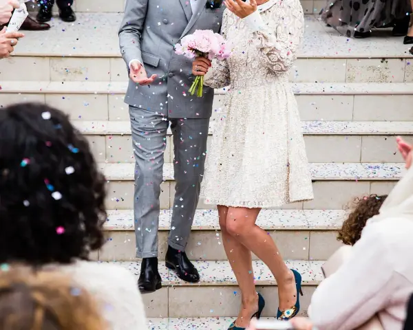 Un couple célèbre sa **danse mariage facile** sous une pluie de confettis. La mariée porte une robe blanche ornée, le marié un costume gris.
