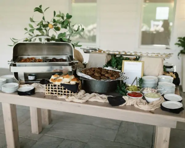Buffet de brunch mariage avec plats chauds, petits pains, garnitures et assiettes empilées.