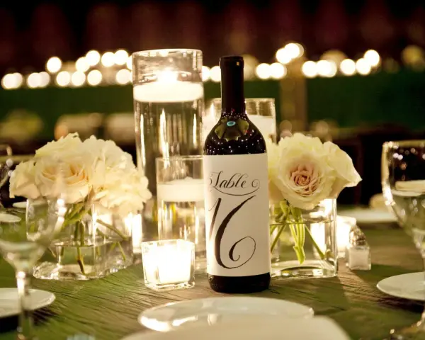 Bouteille de vin avec étiquette "Table 16", entourée de roses pâles, bougies et verres à vin. Parfait pour un dîner avec droit de bouchon traiteur.