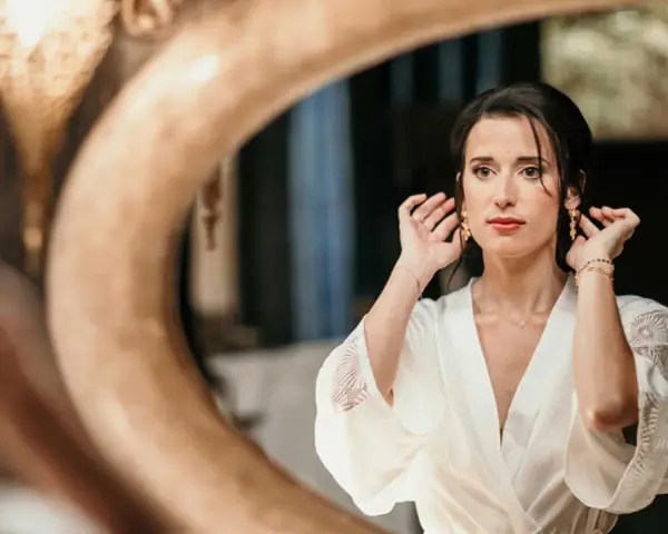 Une mariée, le visage marqué par le stress du mariage, ajuste ses boucles d'oreilles devant un miroir.