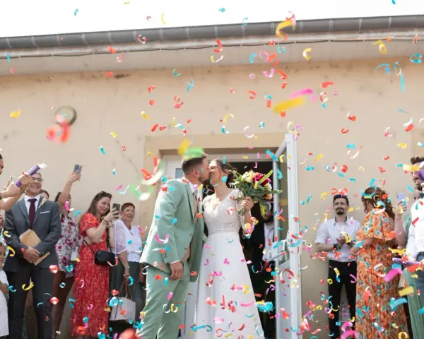 Des confettis colorés pleuvent sur les jeunes mariés qui s'embrassent. Une joyeuse tradition pour célébrer leur union.