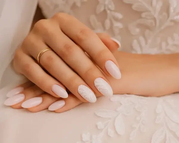 Mains d'une mariée avec des ongles tendance, ornés d'une bague dorée et d'un motif floral délicat sur un ongle.