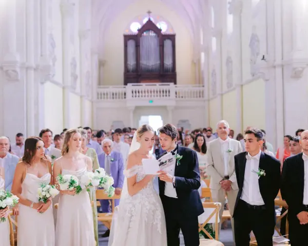 Mariage dans une église : la mariée et le marié lisent un texte, entourés des invités et des demoiselles d'honneur.