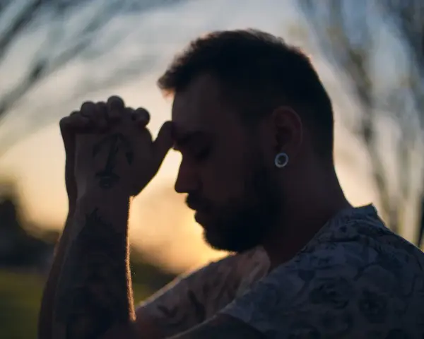Un homme aux mains jointes, le front appuyé sur ses doigts, semble en pleine prière. Son tatouage d'ancre est visible. C'est un moment de prière des époux.