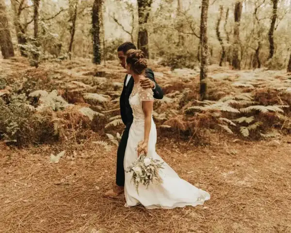 Un couple se promène dans une forêt, la mariée porte une robe blanche et tient un bouquet. Une scène de formalité mariage en pleine nature.