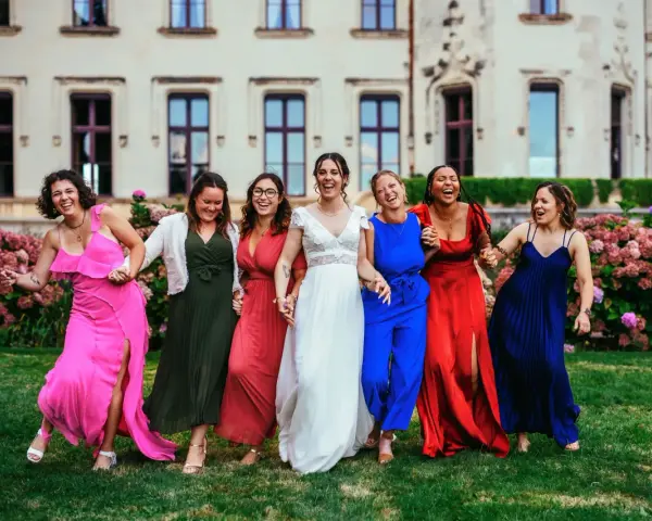 Un groupe de femmes rit joyeusement devant un château. La mariée en blanc est entourée de ses demoiselles d'honneur en robes colorées. La différence entre témoin et demoiselle d'honneur est subtile, mais leur complicité est évidente.