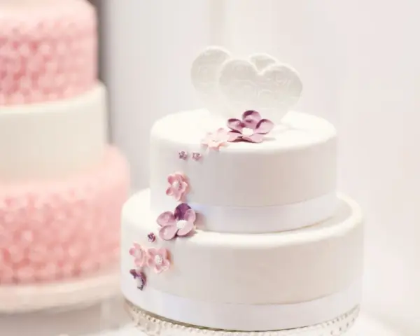Deux pièces montées, l'une blanche décorée de cœurs et fleurs, l'autre rose texturée. Le coût d'une pièce montée peut varier.