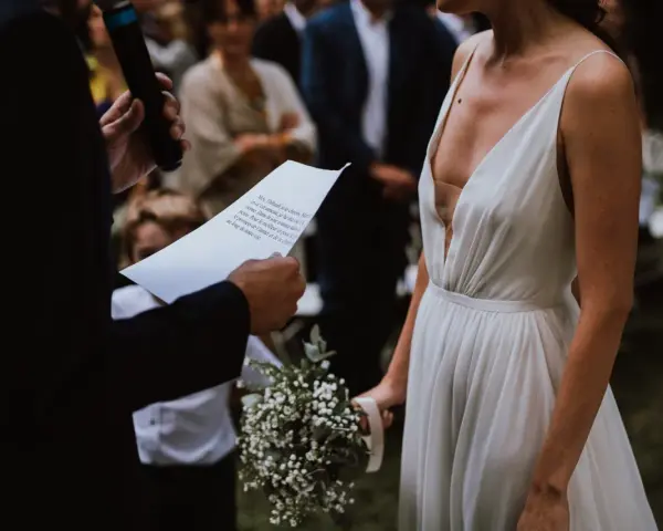 La mariée en robe blanche, bouquet à la main, écoute les vœux lors de son mariage religieux.