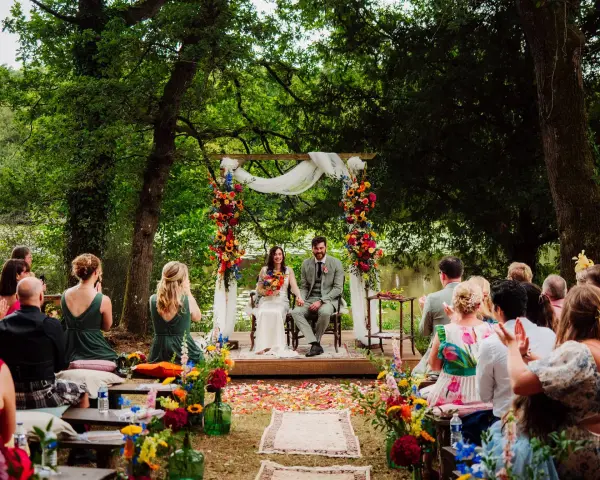 Un couple souriant lors d'une cérémonie laïque en plein air, entouré de verdure et de fleurs colorées. L'officiant cérémonie laïque guide ce moment unique.