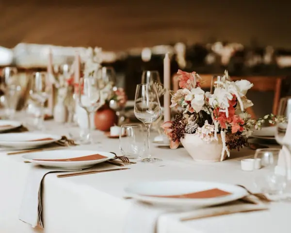 Un plan de table mariage élégant : vaisselle, verres, bougies et un bouquet de fleurs sur une table dressée.