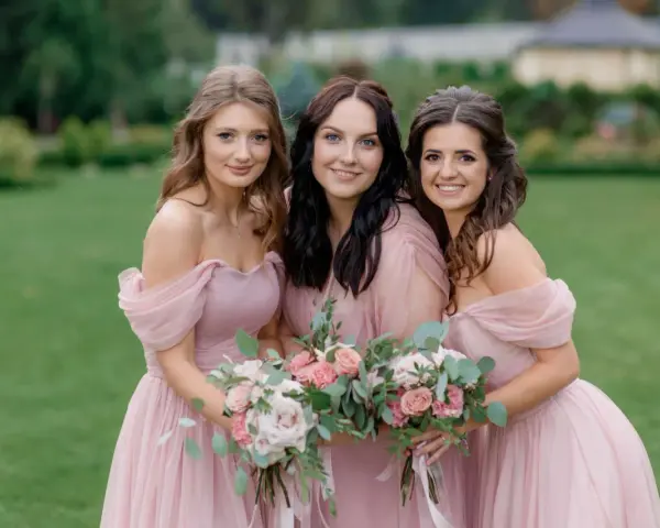 Trois demoiselles d'honneur souriantes en robes roses, tenant des bouquets de fleurs. Une belle scène pour une demande demoiselle d'honneur.