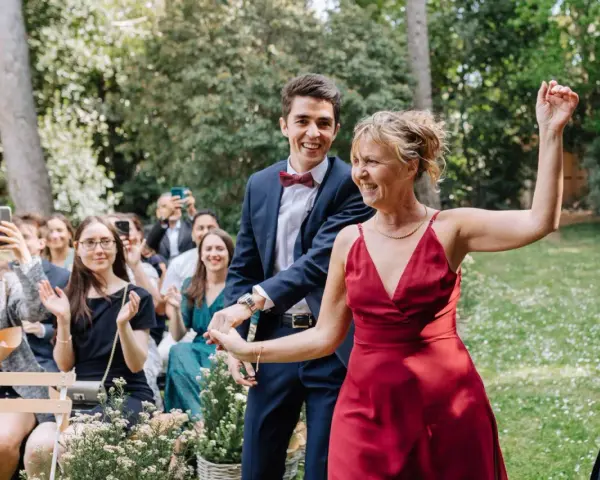 Un couple rayonnant danse lors d'un cortege mariage en plein air. La foule applaudit et filme ce moment joyeux.