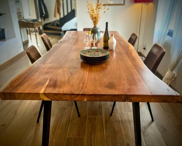 Table rectangulaire en bois massif, prête pour un repas festif dans une salle des fêtes. Assiettes décorées, verres et bouteille attendent les convives.