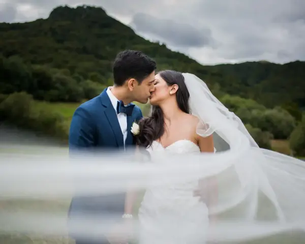 Un couple s'embrasse, le voile de la mariée flottant au vent. Une scène romantique qui donne envie de savoir comment organiser un mariage.