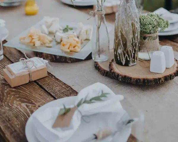 Table setting rustique pour une préparation de cérémonie laïque : assiettes, verres, plateau de fromages, cadeaux et décoration florale.
