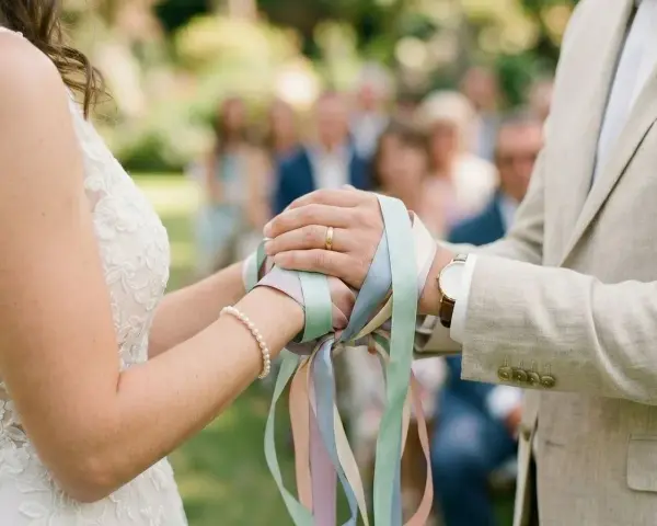 Mains jointes, rubans pastel noués, symbole d'un rituel d'union. Le couple célèbre son amour.
