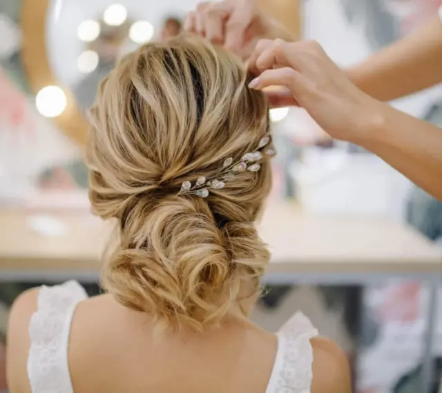 Une coiffure mariage chic avec un chignon flou orné d'une barrette scintillante. Les mains d'une coiffeuse ajustent les dernières mèches.