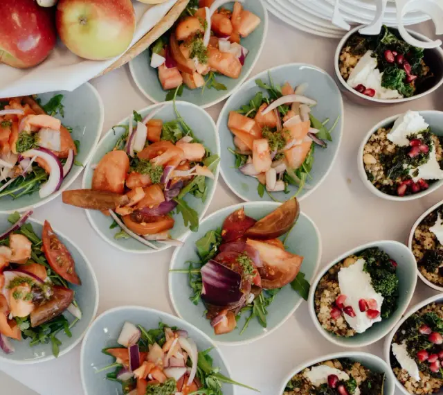 Petits plats individuels de salades de tomates et d'oignons rouges, et de quinoa aux légumes, prêts pour un repas de mariage.