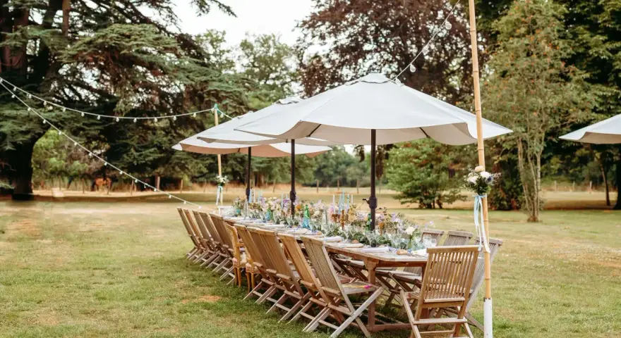 Table dressée pour un mariage jardin, avec des chaises en bois, des parasols et des guirlandes lumineuses.