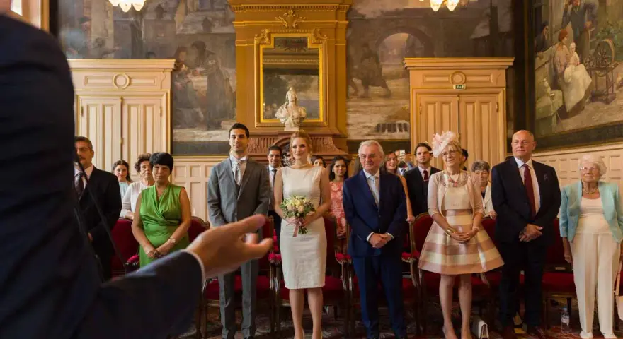 Le couple se tient au centre, entouré de leurs 5 témoins mariage. La mariée porte une robe blanche et tient un bouquet. Les invités sont élégamment vêtus.