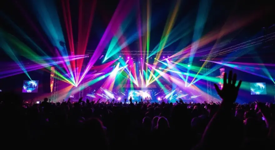 Une foule en délire sous un **totem jeux de lumière** spectaculaire, des faisceaux multicolores illuminent la scène et le public.