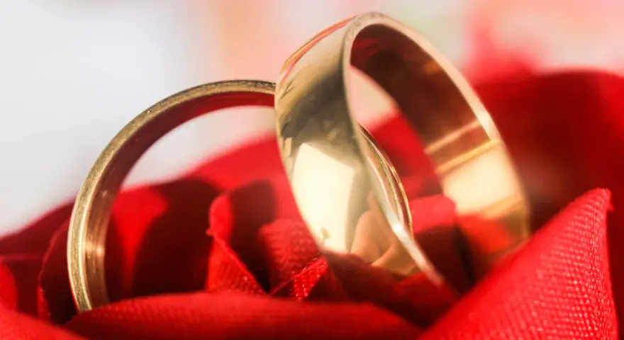 Deux alliances dorées reposent sur un tissu rouge, symbolisant l'amour et l'organisation mariage.