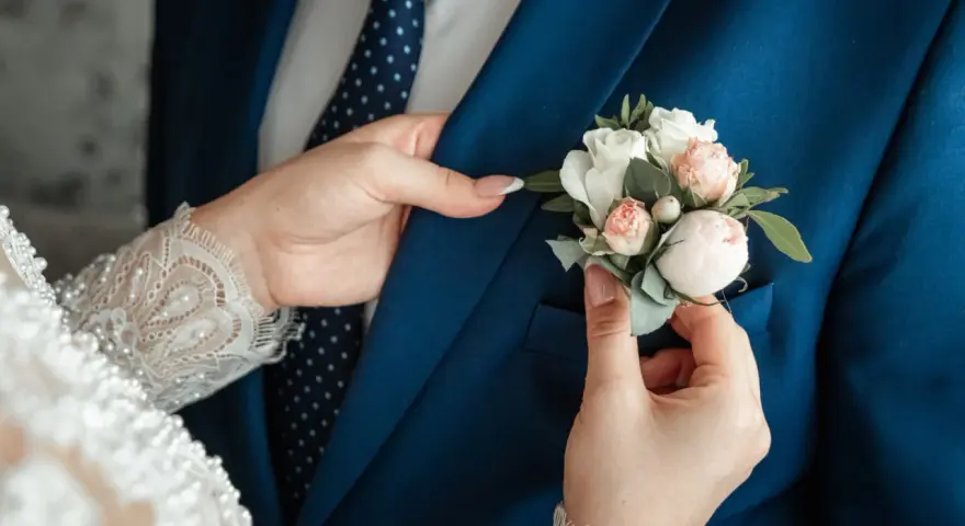 Les mains délicates de la mariée ajustent la boutonnière sur le costume bleu du marié, un symbole de leur mariage avec un étranger.