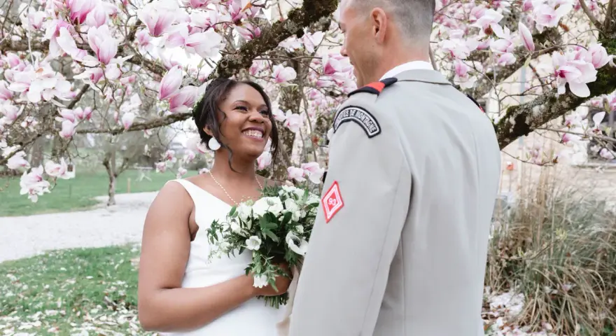 Un couple rayonnant lors de leur mariage militaire, sous un magnolia en fleurs.