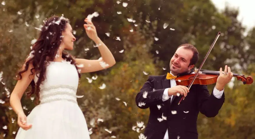 Une mariée en robe blanche danse sous une pluie de plumes, tandis que son mari joue du violon. Une scène féerique pour un mariage champêtre.