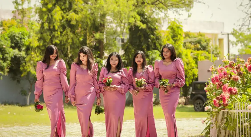 Cinq demoiselles d'honneur en robes roses marchent ensemble, tenant des bouquets.