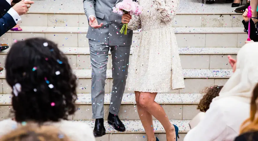 Un couple célèbre sa **danse mariage facile** sous une pluie de confettis. La mariée porte une robe blanche ornée, le marié un costume gris.