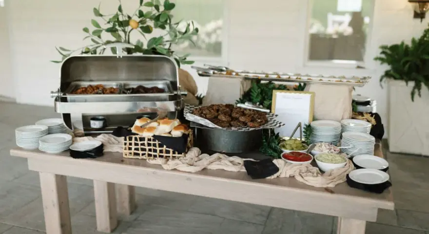 Buffet de brunch mariage avec plats chauds, petits pains, garnitures et assiettes empilées.