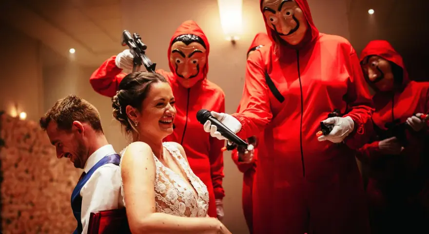 Une mariée hilare, un micro tendu par un personnage masqué rouge. Une scène inattendue pour un mariage surprise.