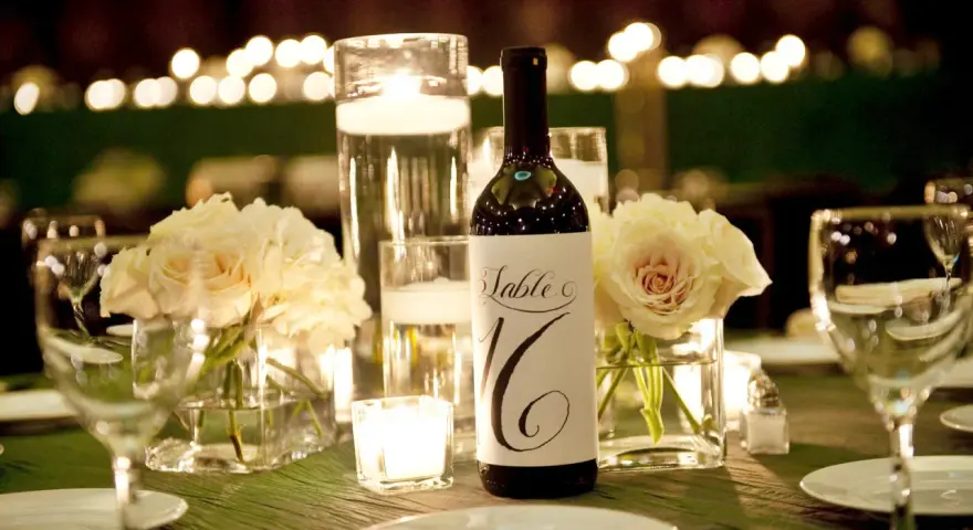 Bouteille de vin avec étiquette "Table 16", entourée de roses pâles, bougies et verres à vin. Parfait pour un dîner avec droit de bouchon traiteur.