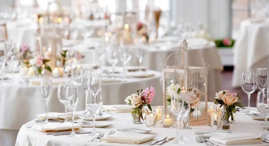 Un élégant plan de table mariage en U, avec des tables rondes dressées de vaisselle fine, de verres à pied, de bougies et de bouquets de roses.