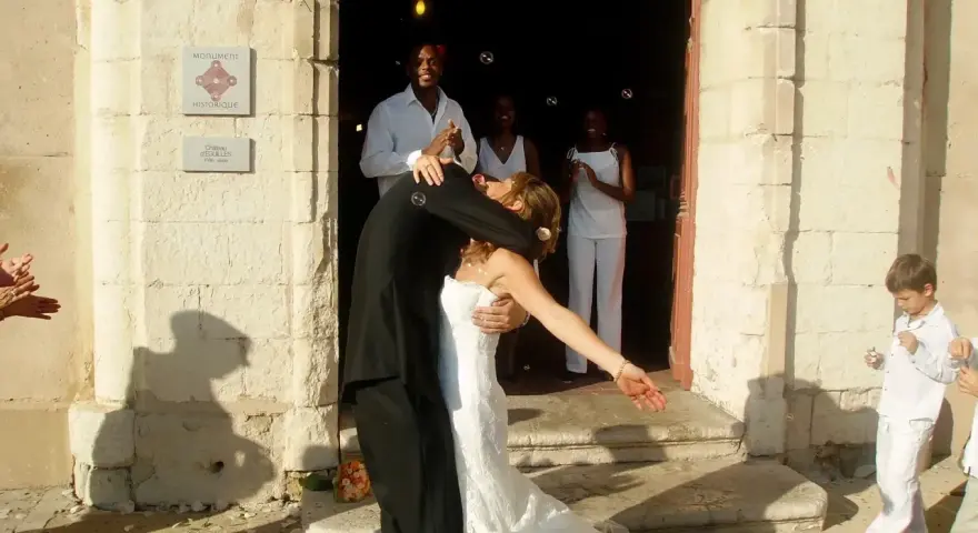 Mariage à l'église : le couple s'embrasse devant l'édifice, entouré d'invités joyeux. La musique du mariage résonne.