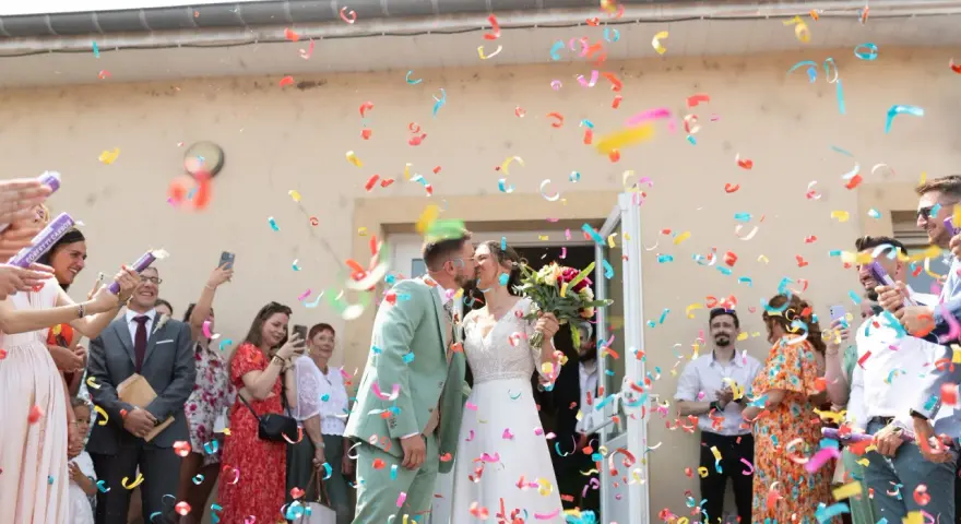 Des confettis colorés pleuvent sur les jeunes mariés qui s'embrassent. Une joyeuse tradition pour célébrer leur union.