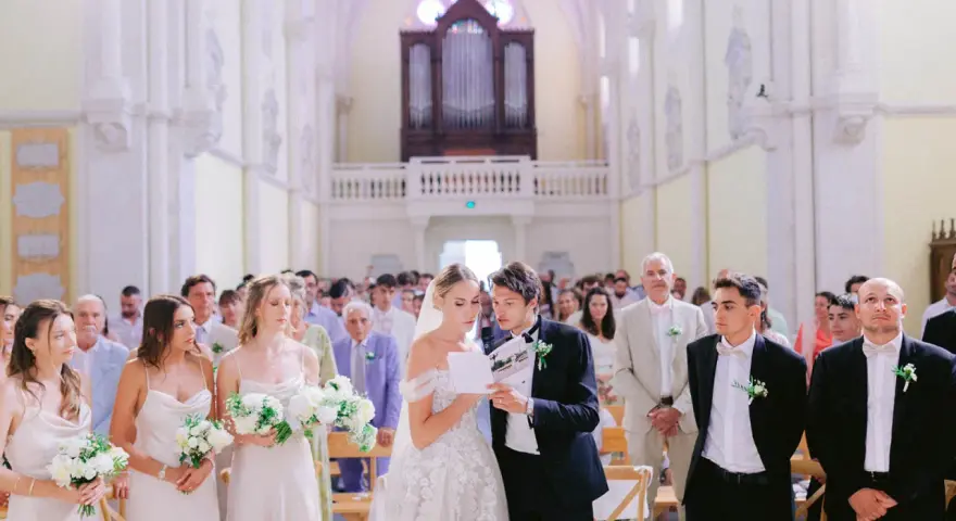 Mariage dans une église : la mariée et le marié lisent un texte, entourés des invités et des demoiselles d'honneur.