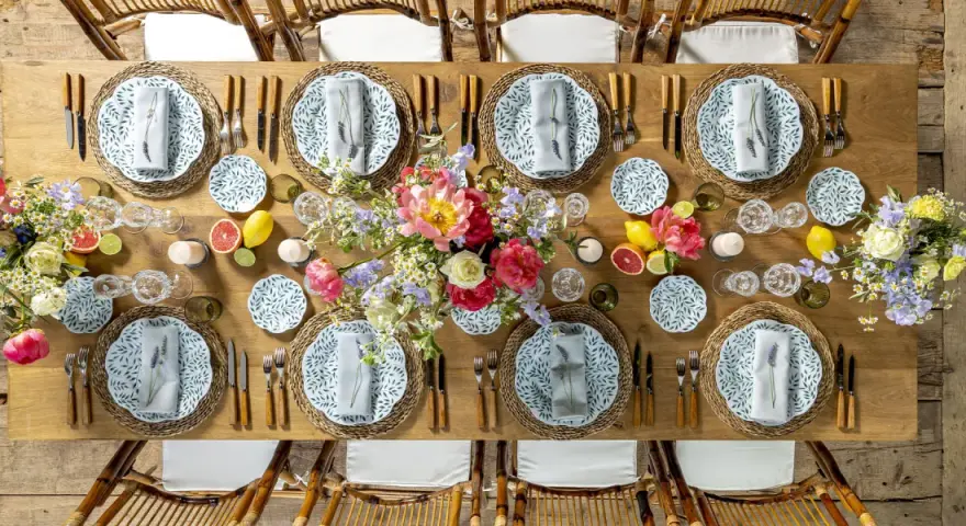 Plan de salle mariage table ronde : une table en bois dressée avec des assiettes fleuries, des verres en cristal, des fruits et des bouquets de fleurs.