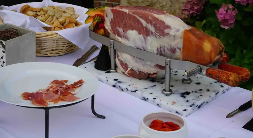 Un jambon cru entier prêt à être découpé, accompagné de pain et de fruits, pour un vin d'honneur original.