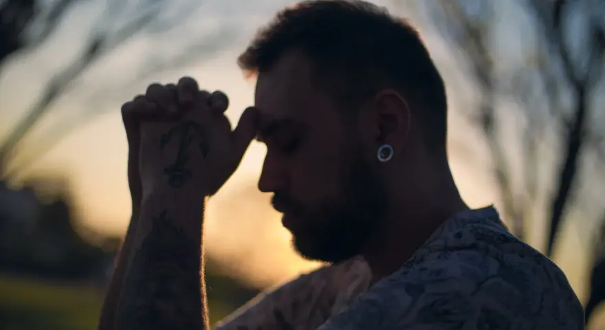 Un homme aux mains jointes, le front appuyé sur ses doigts, semble en pleine prière. Son tatouage d'ancre est visible. C'est un moment de prière des époux.