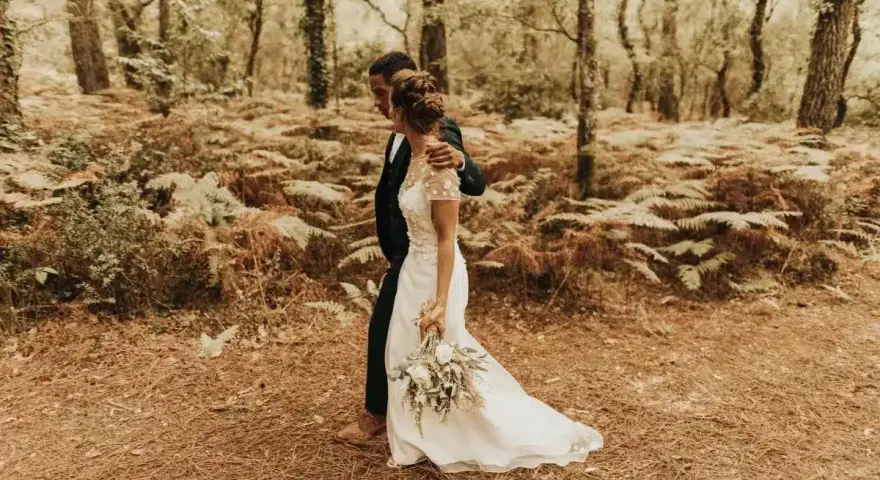 Un couple se promène dans une forêt, la mariée porte une robe blanche et tient un bouquet. Une scène de formalité mariage en pleine nature.