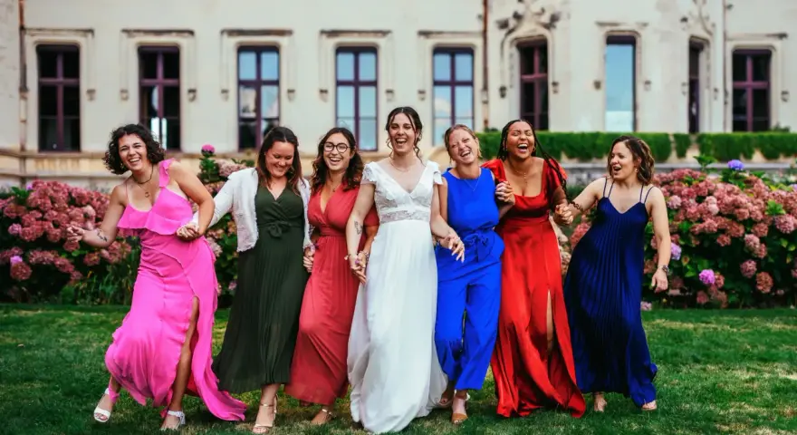Un groupe de femmes rit joyeusement devant un château. La mariée en blanc est entourée de ses demoiselles d'honneur en robes colorées. La différence entre témoin et demoiselle d'honneur est subtile, mais leur complicité est évidente.