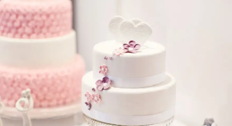 Deux pièces montées, l'une blanche décorée de cœurs et fleurs, l'autre rose texturée. Le coût d'une pièce montée peut varier.
