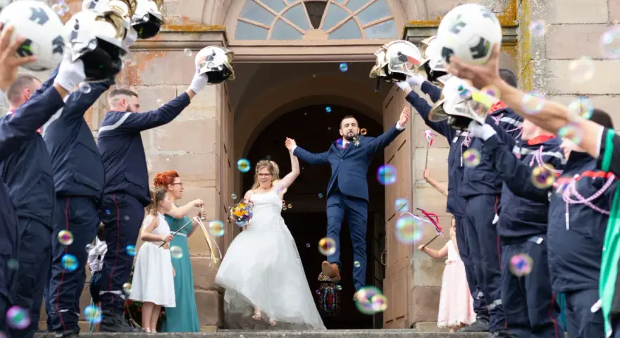 Mariés sortant de l'église sous une haie d'honneur mariage de pompiers lançant des bulles.