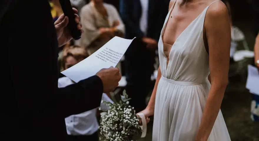 La mariée en robe blanche, bouquet à la main, écoute les vœux lors de son mariage religieux.
