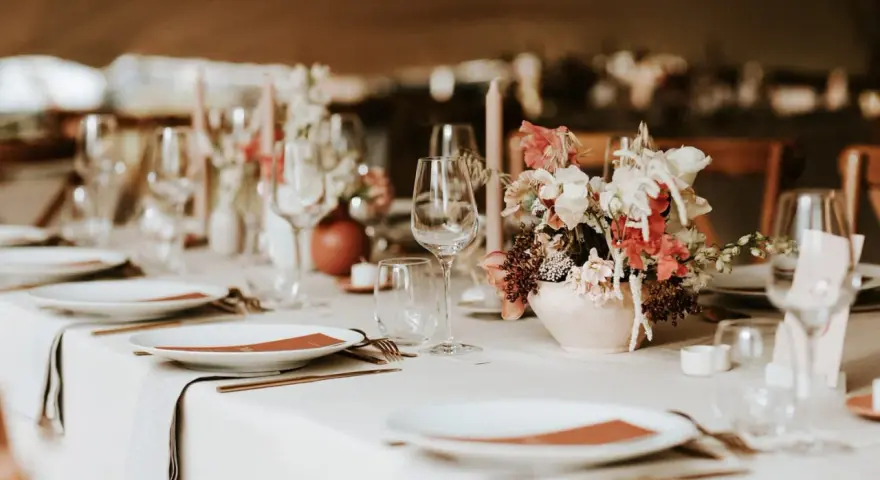 Un plan de table mariage élégant : vaisselle, verres, bougies et un bouquet de fleurs sur une table dressée.